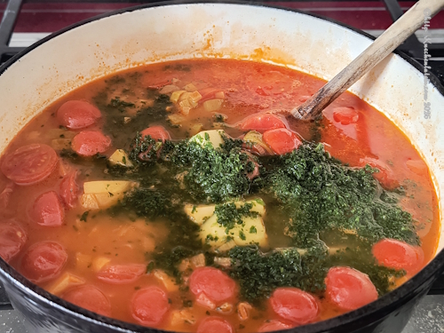 Kochtopf mit Eintopf mit Kichererbsen, Kartoffeln und Tomaten, darin ein Holzlöffel