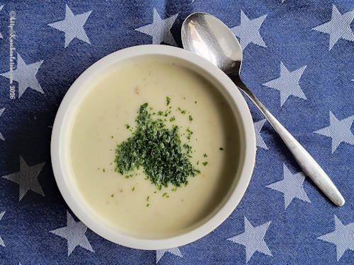 Eine Suppenschale Käse-Kartoffelsuppe mit Petersilie garniert, daneben ein Esslöffel