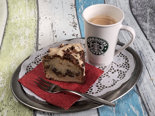 Ein Stück Sauerrahm Kaffeekuchen mit Kuchengabel neben einer Tasse Kaffe